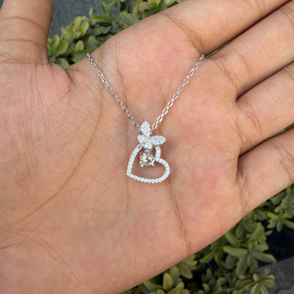 Silver necklace with a heart and angel pendant held in a hand against a natural background