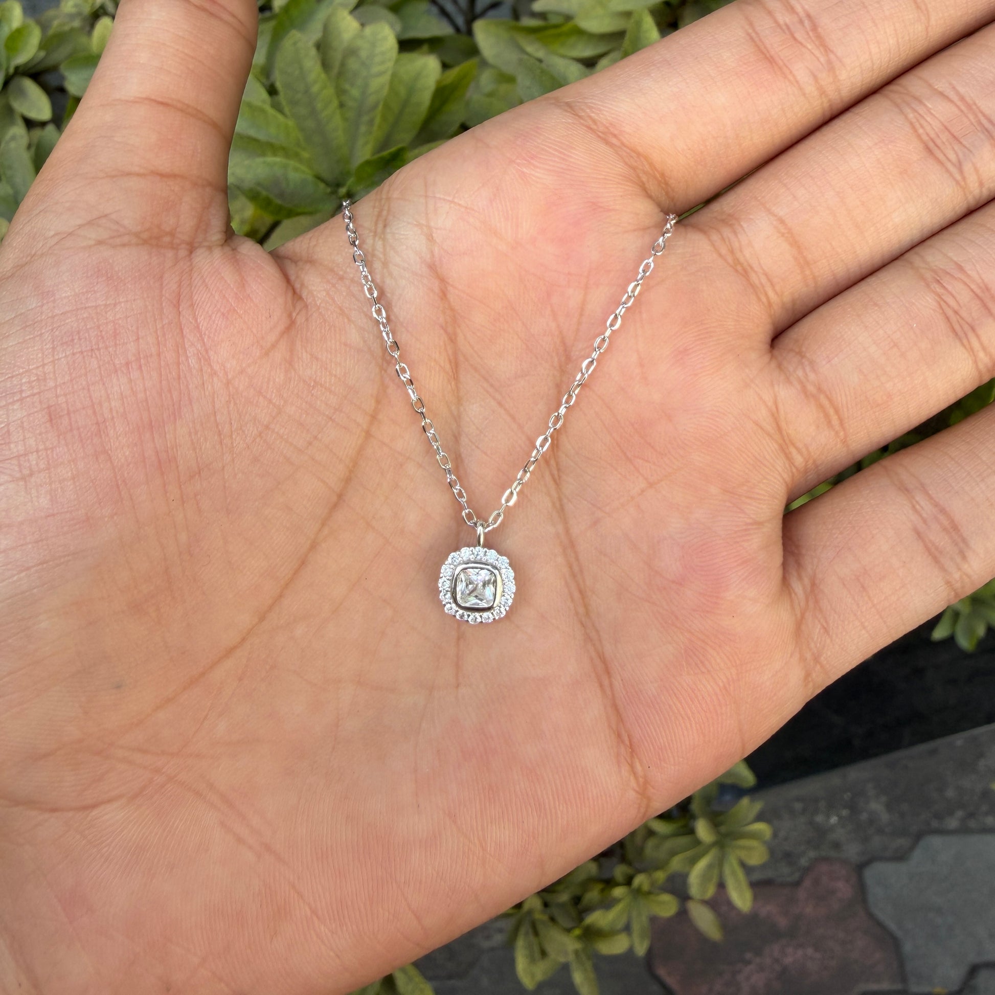 Silver necklace with a pendant on a hand against a green leafy background