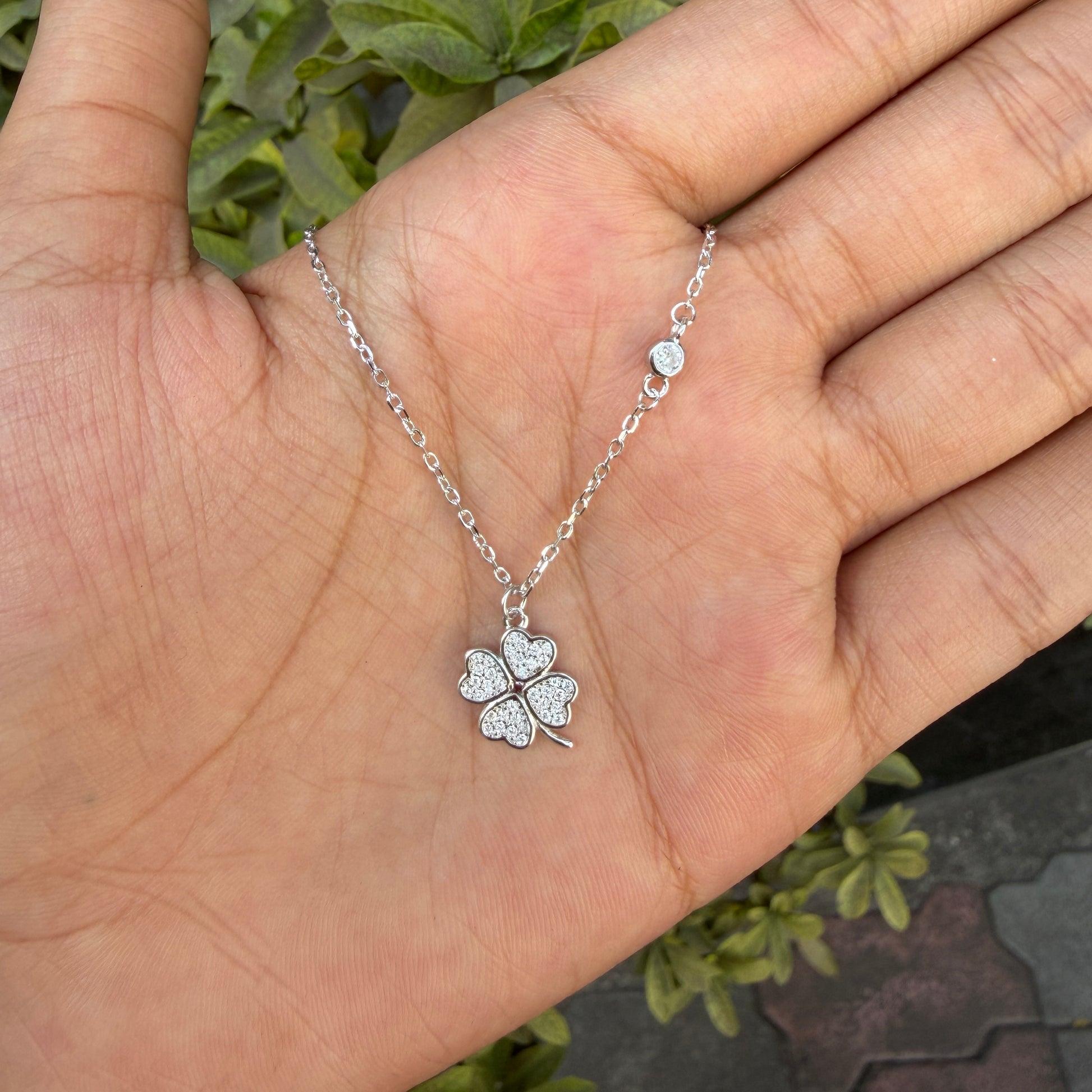 Silver four-leaf clover necklace on a hand with a blurred green background