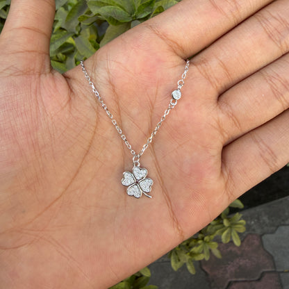 Silver four-leaf clover necklace on a hand with a blurred green background