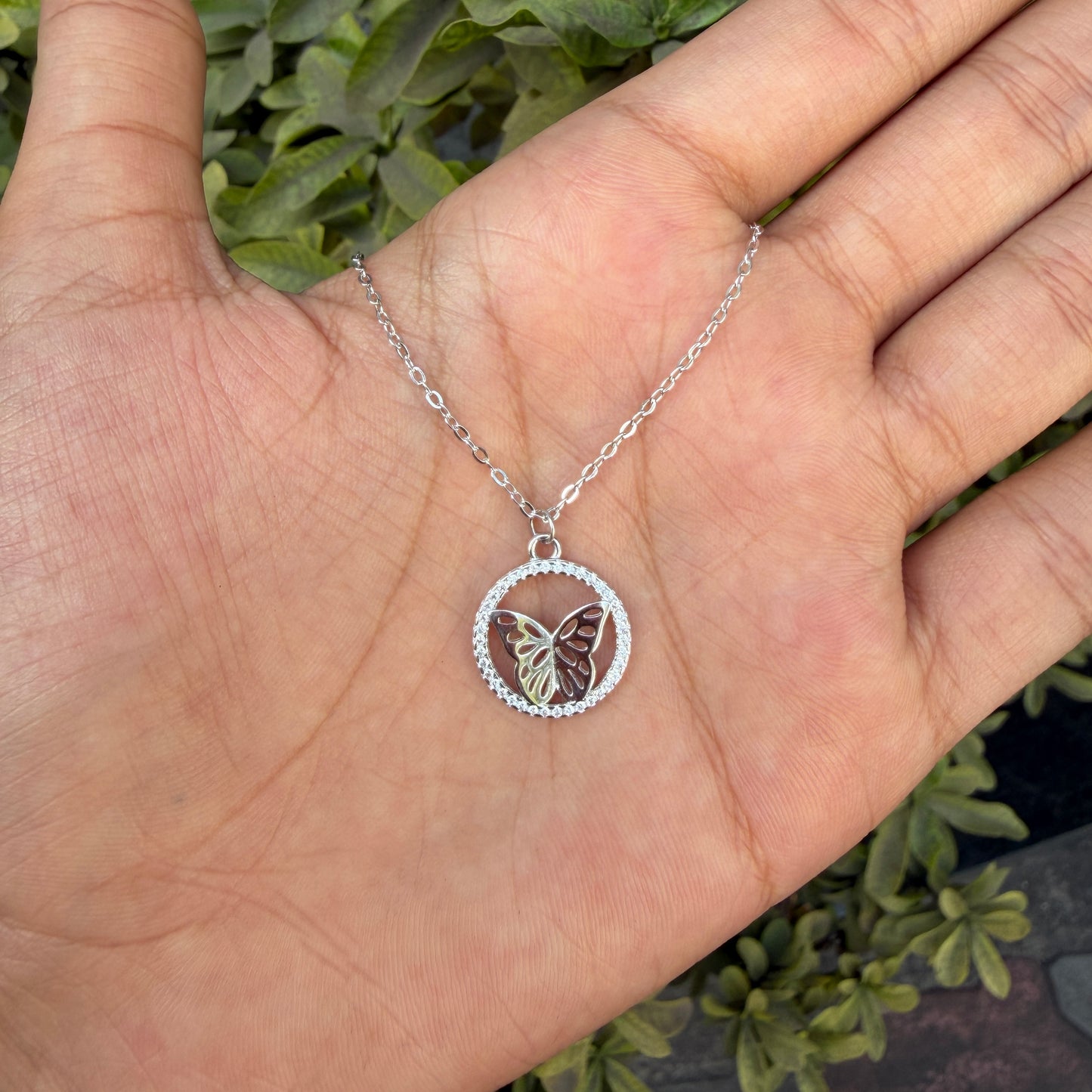 Silver necklace with a butterfly pendant held in a hand against a natural background
