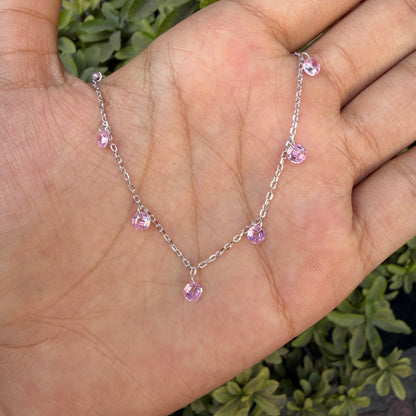 Silver necklace with pink gemstones on a hand against a green plant background