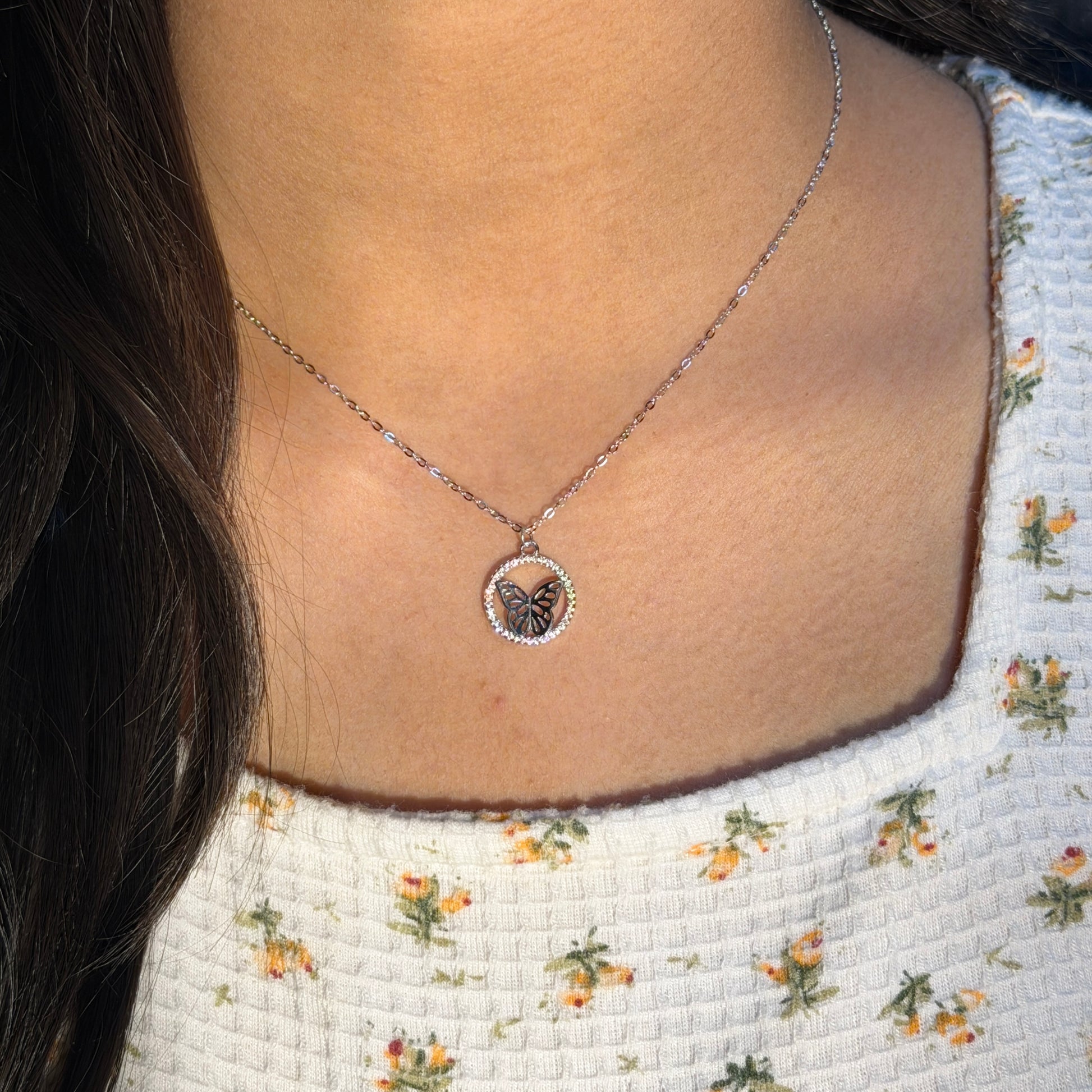 Necklace with a butterfly pendant worn by a person against a floral-patterned background