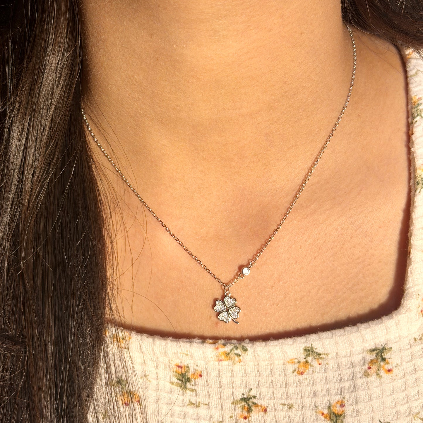 Necklace with a clover pendant worn by a person with floral-patterned clothing.