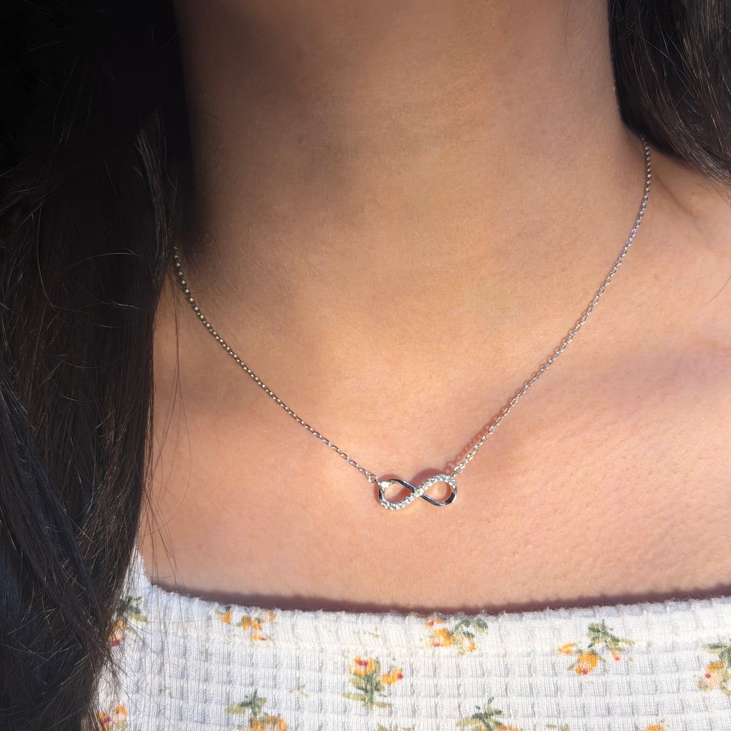 Necklace with an infinity symbol pendant worn by a person with floral-patterned clothing.