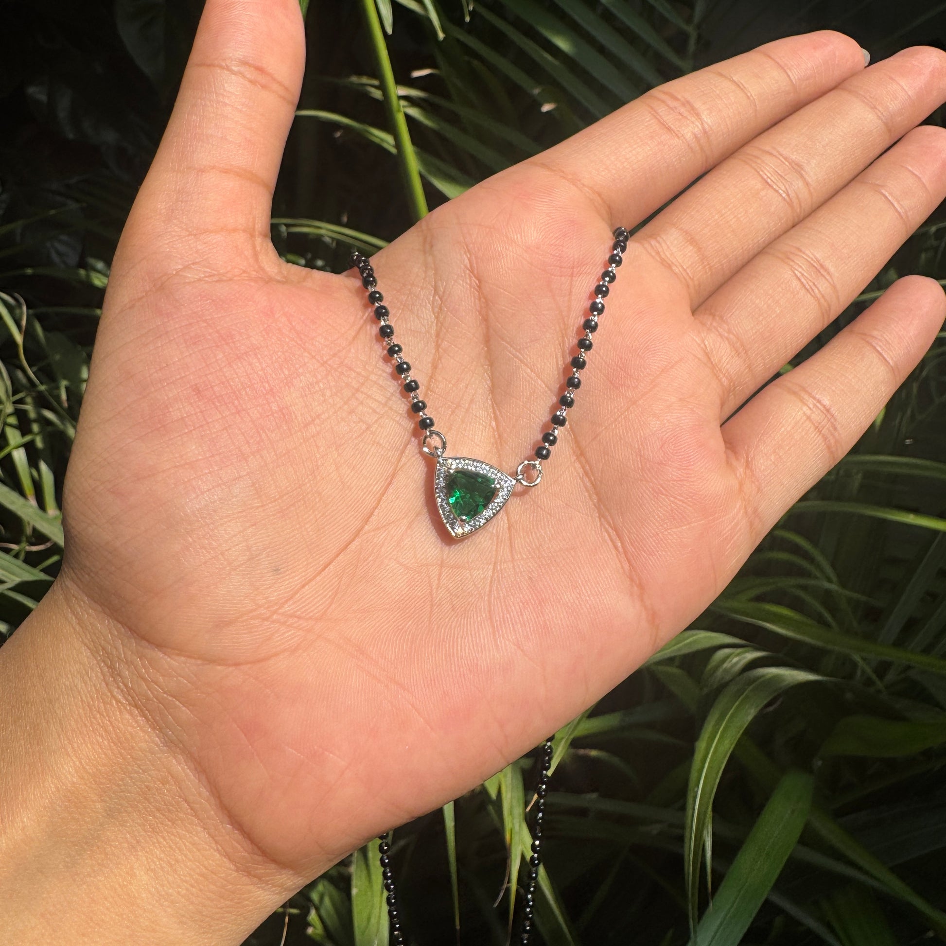 Hand holding a necklace with a green heart pendant against a leafy background