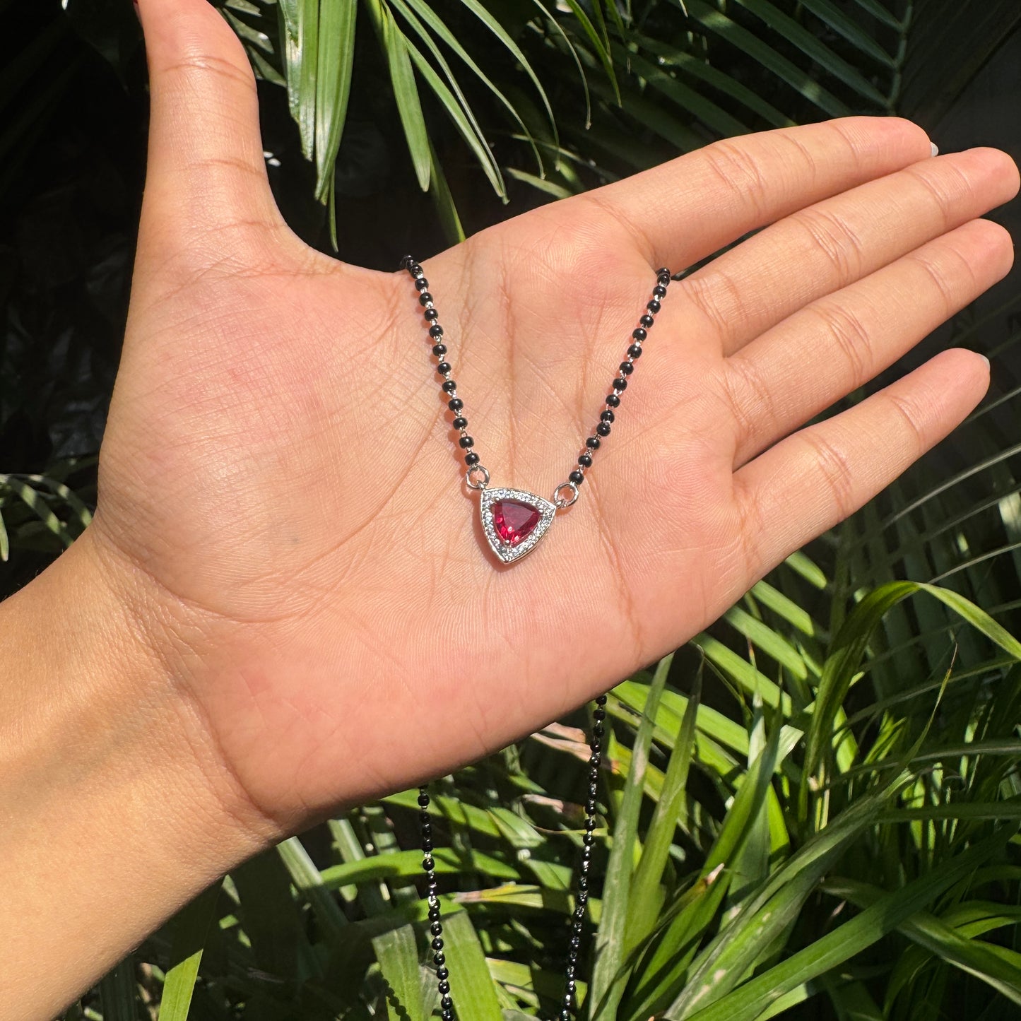 Necklace with a heart-shaped red gemstone pendant held in a hand against a green leafy background