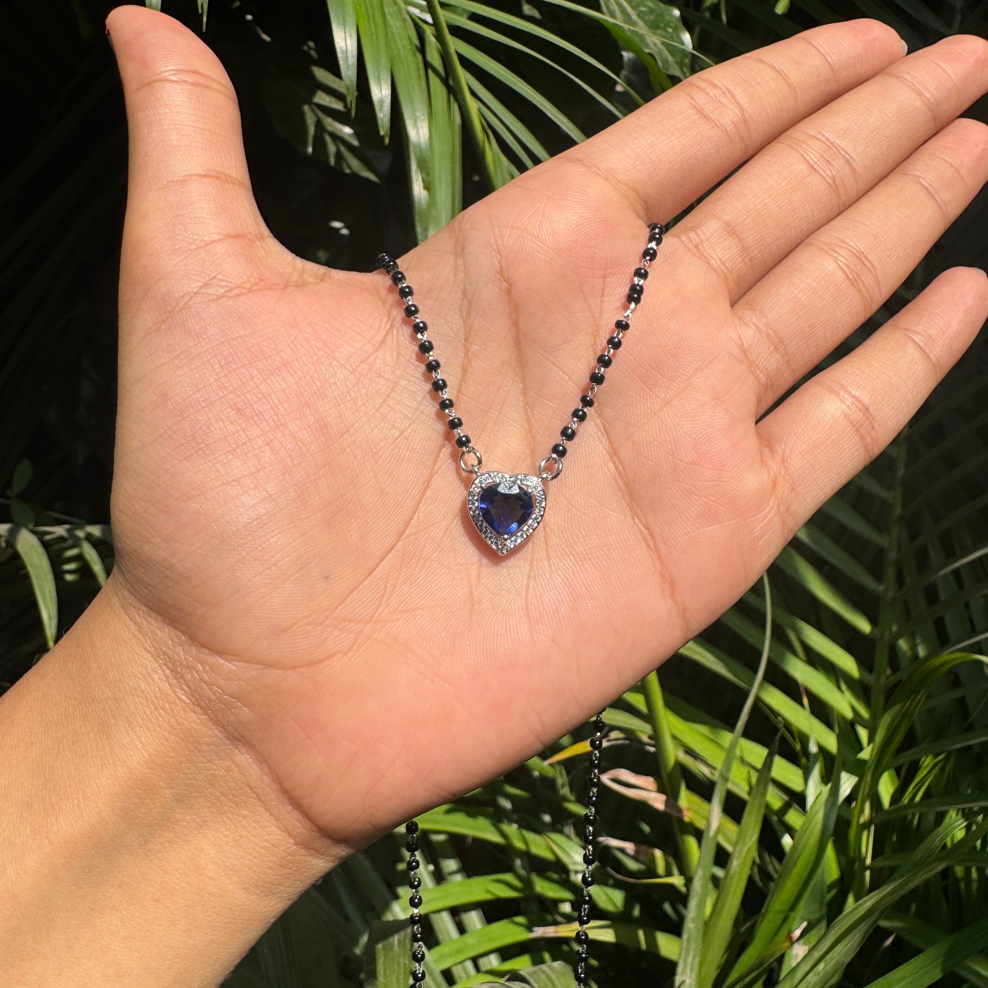 Necklace with a heart-shaped purple gemstone held in a hand against a leafy background