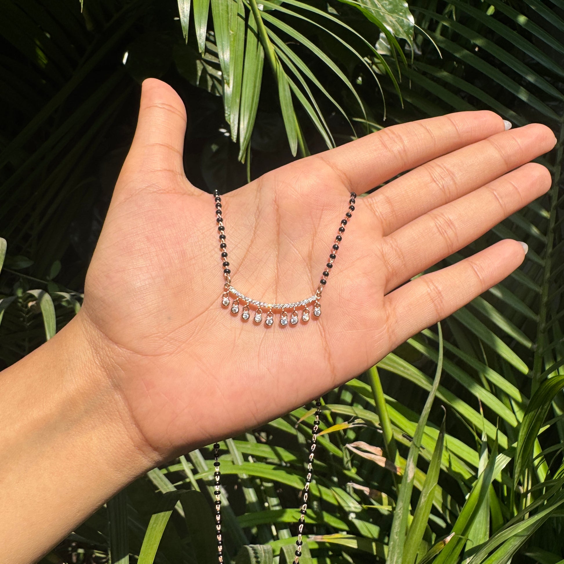 Hand holding a necklace with green leaves in the background