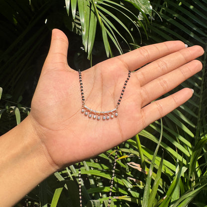 Hand holding a necklace with green leaves in the background