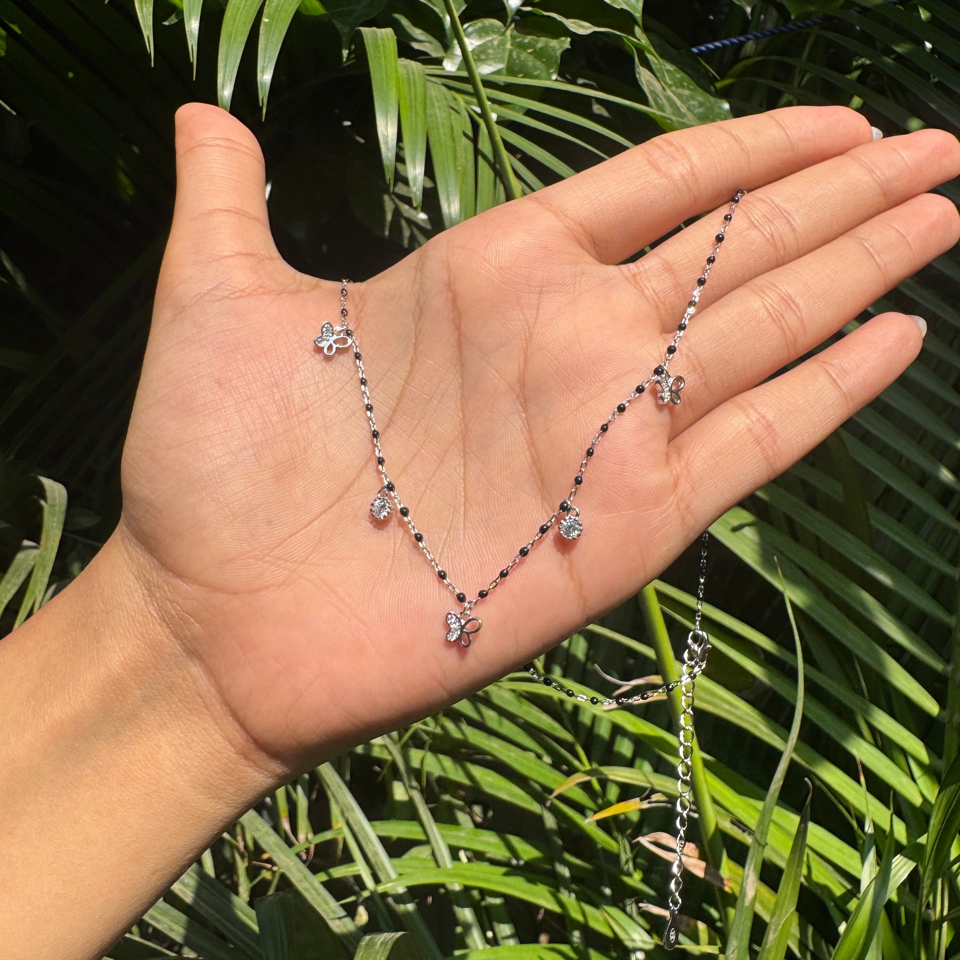 Hand holding a delicate necklace with green leaves in the background
