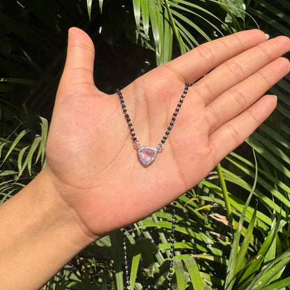 Necklace with a heart-shaped pink pendant held in a hand against a green leafy background
