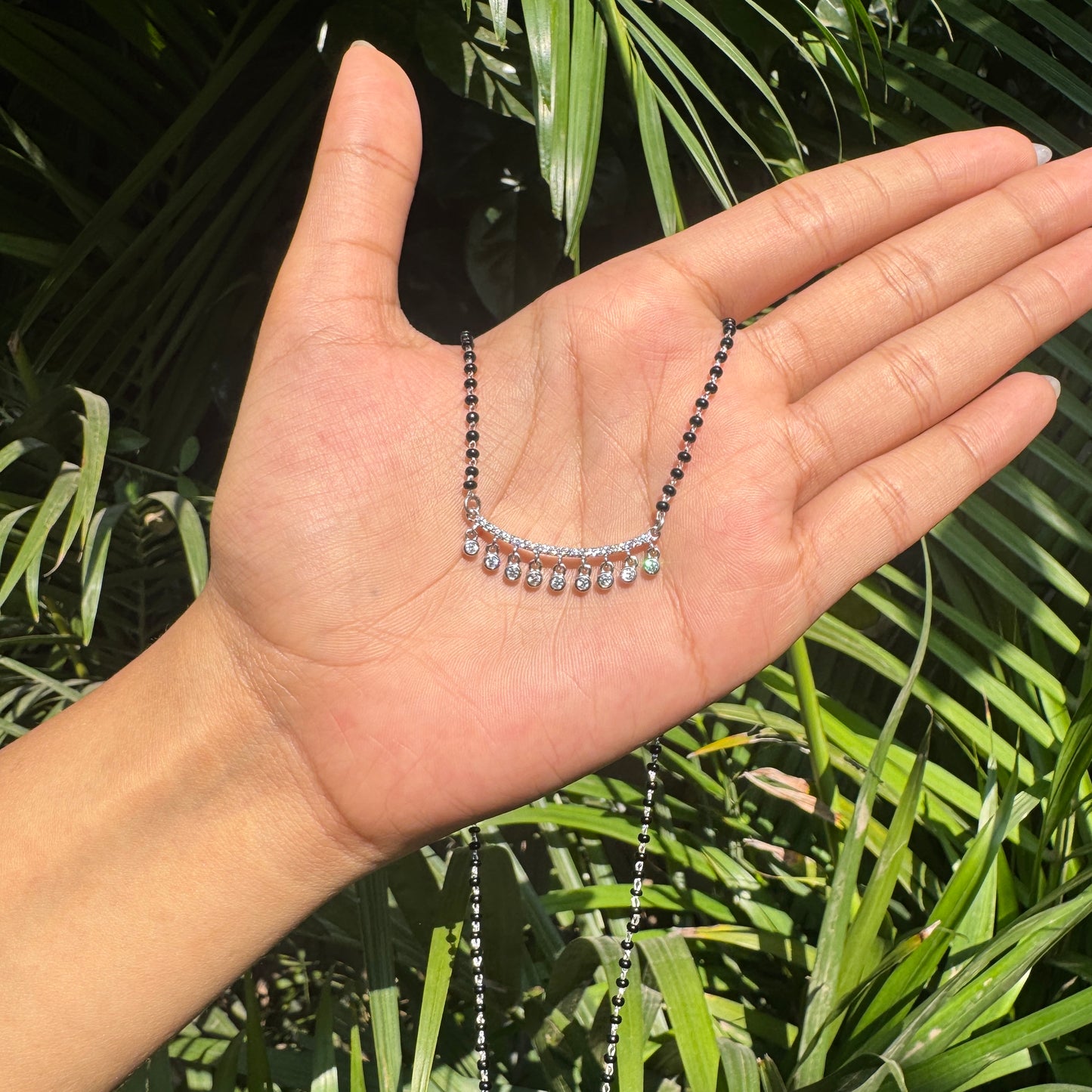Hand holding a necklace with green leaves in the background