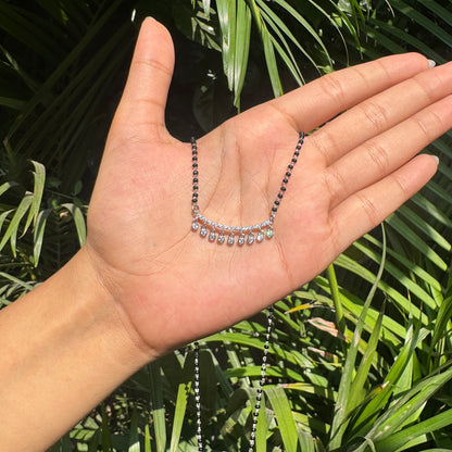 Hand holding a necklace with green leaves in the background