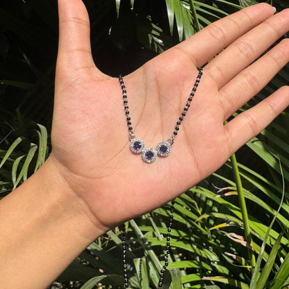 Hand holding a necklace with green leaves in the background