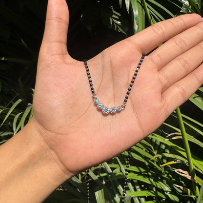 Necklace with blue stones held in a hand against a leafy background