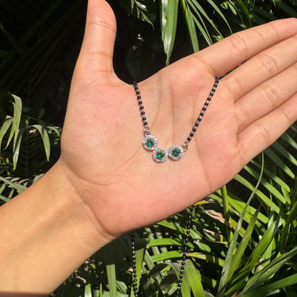 Hand holding a necklace with green gemstones against a leafy background