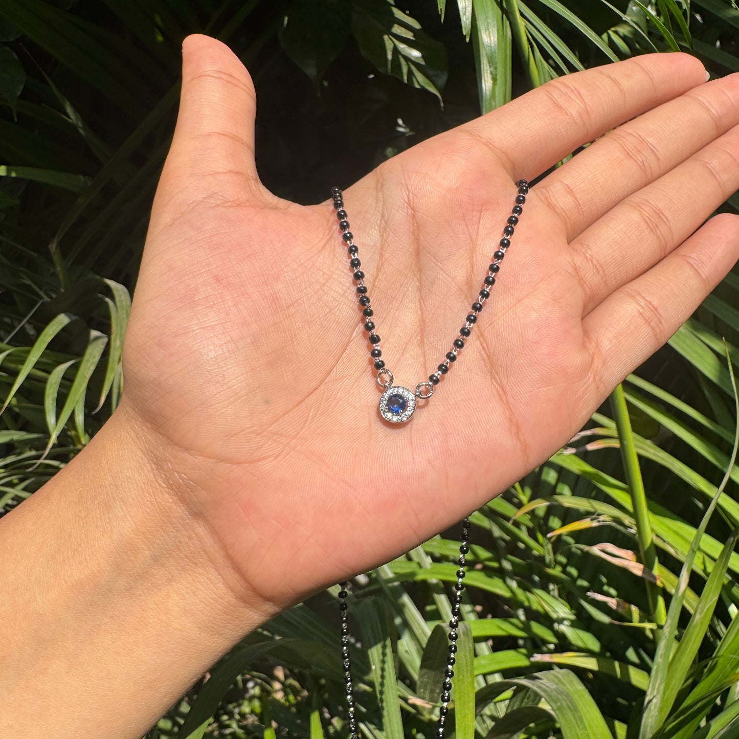 Necklace with a blue gemstone held in a hand against a green leafy background