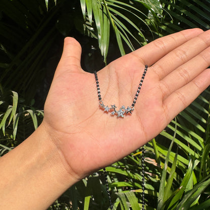 Hand holding a necklace with star-shaped pendants against a leafy background