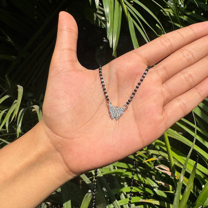Hand holding a necklace with a leaf-shaped pendant against a green leafy background