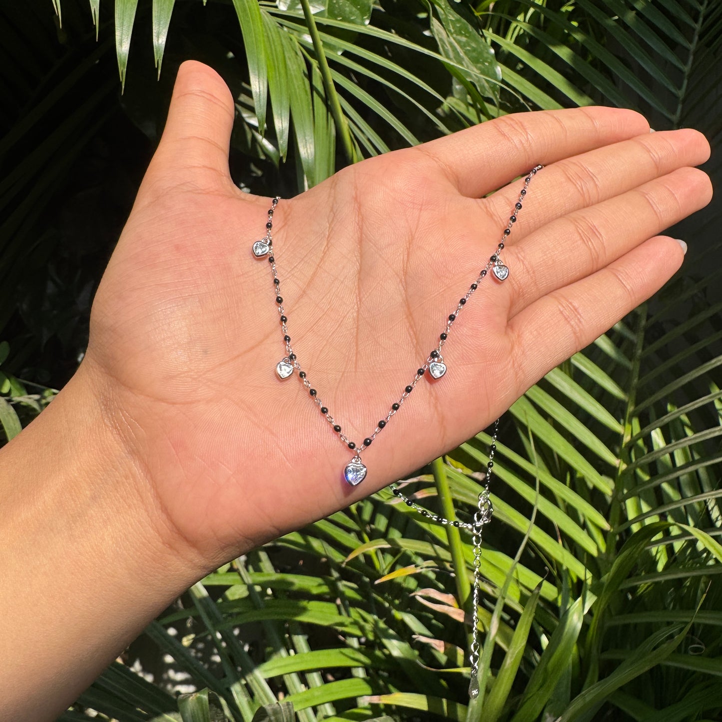 Necklace held in a hand with a green leafy background
