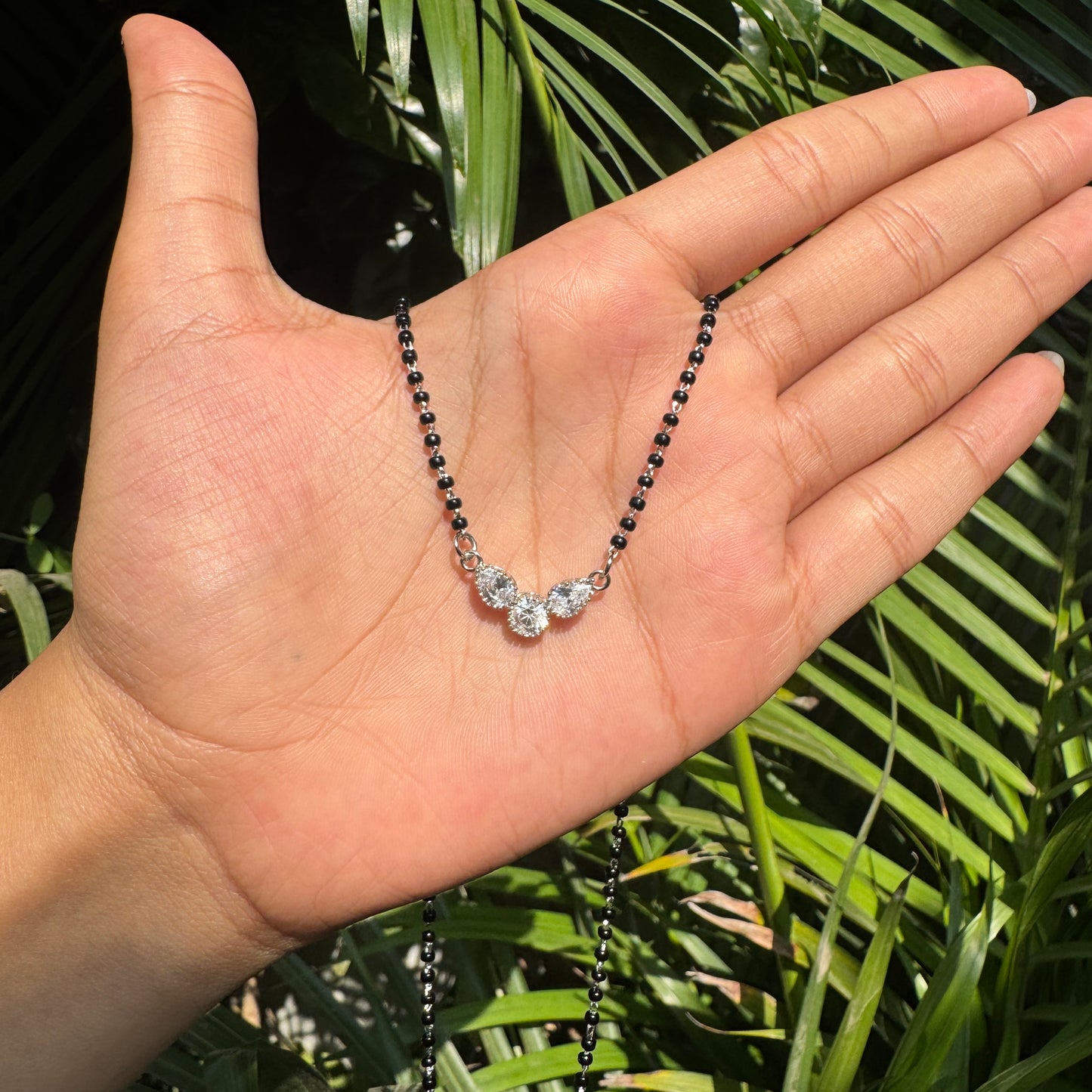 Hand holding a necklace with green leaves in the background