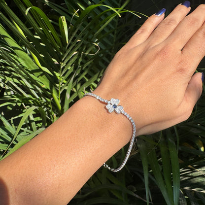 Hand wearing a silver bracelet with a floral design against a green leafy background