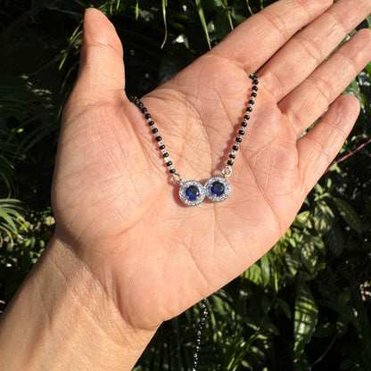 Hand holding a necklace with blue gemstones against a natural background