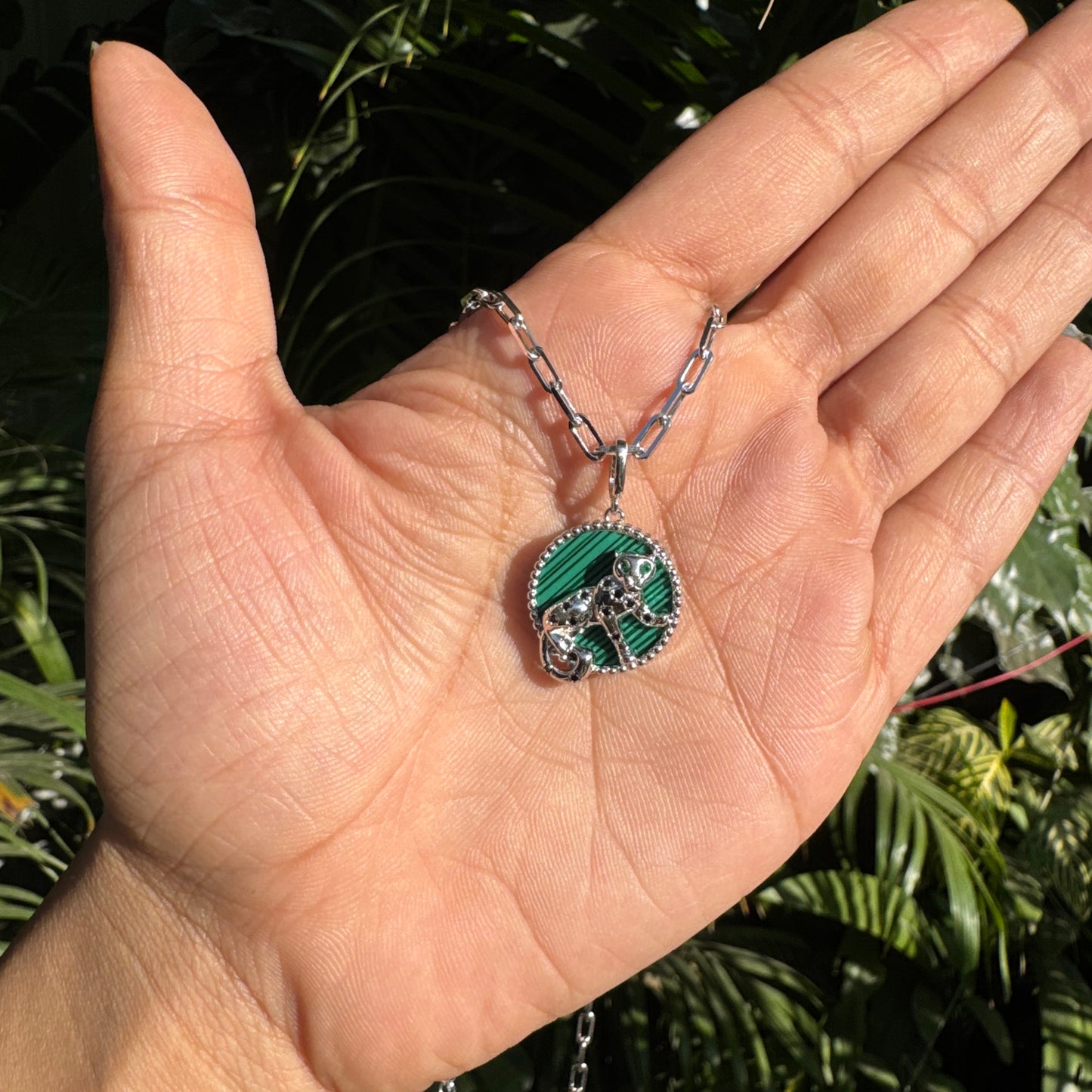 Hand holding a necklace with a green pendant against a natural background