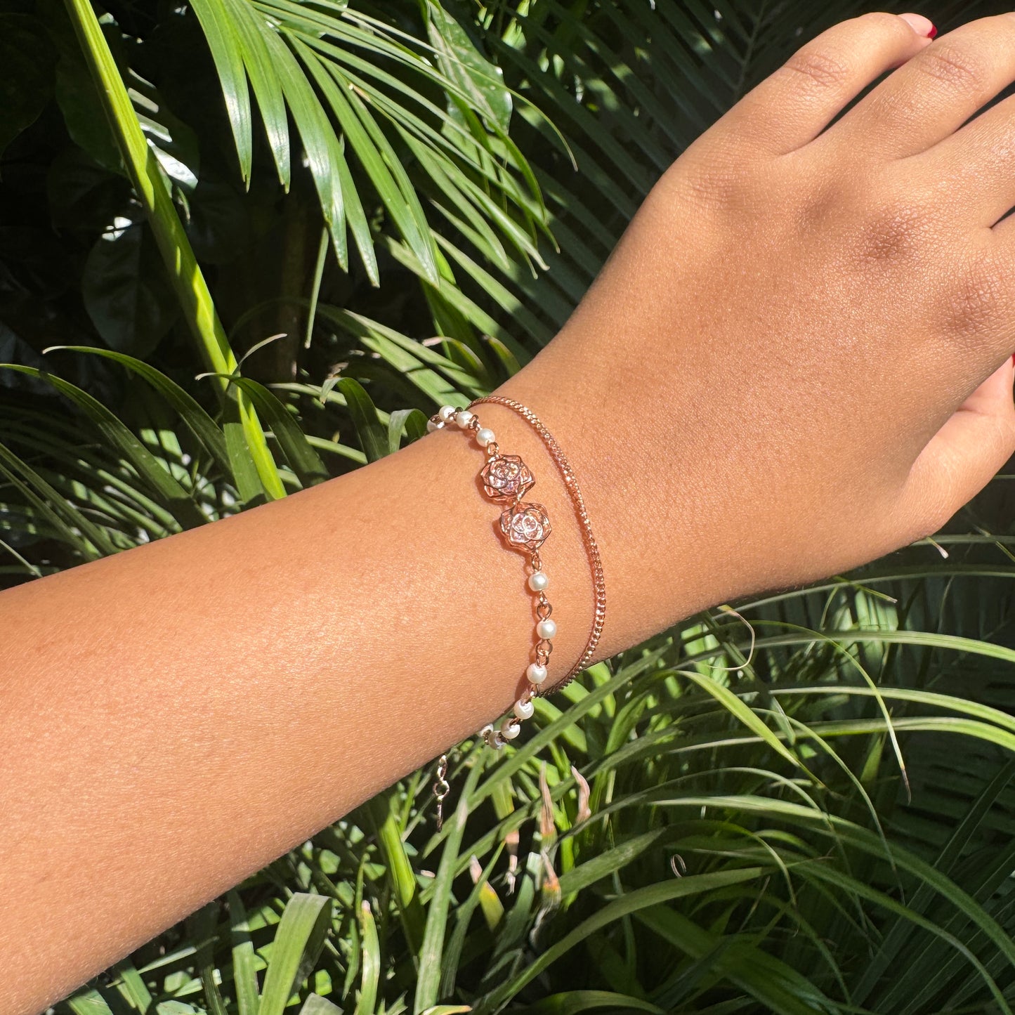 Hand wearing a bracelet with green foliage in the background