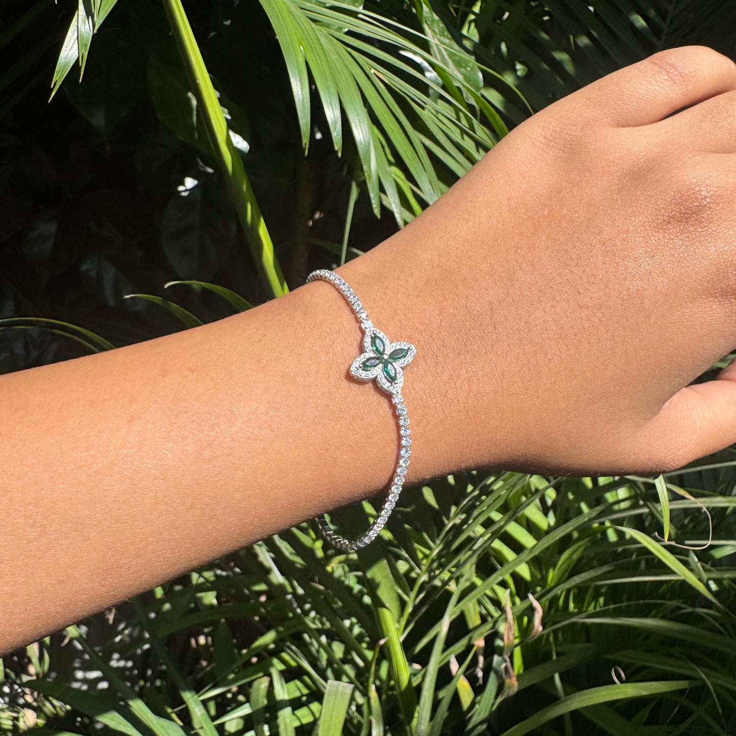 Hand wearing a bracelet with a butterfly charm against a green leafy background