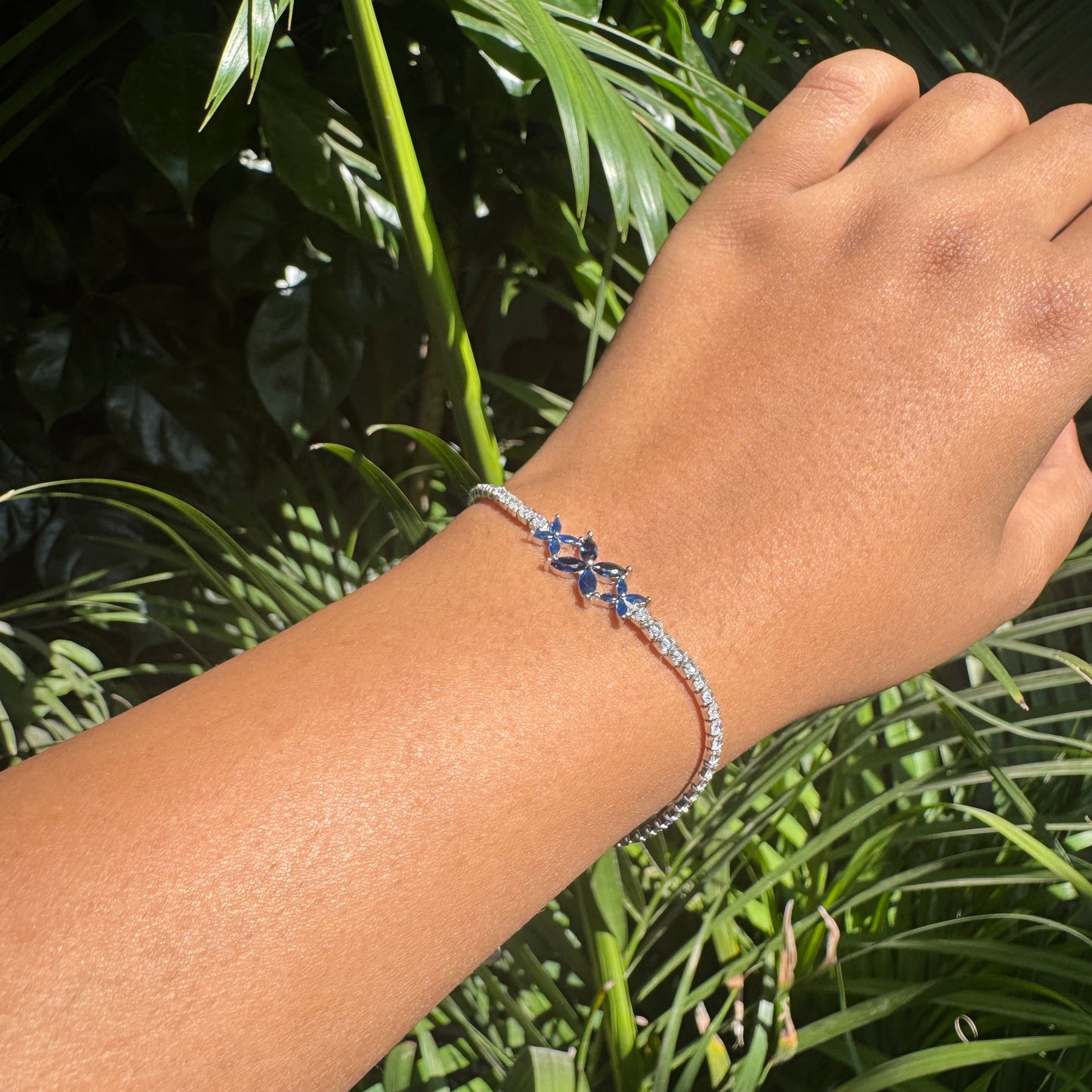 Hand wearing a bracelet with blue flowers against a green leafy background