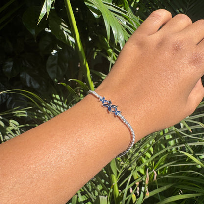Hand wearing a bracelet with blue flowers against a green leafy background
