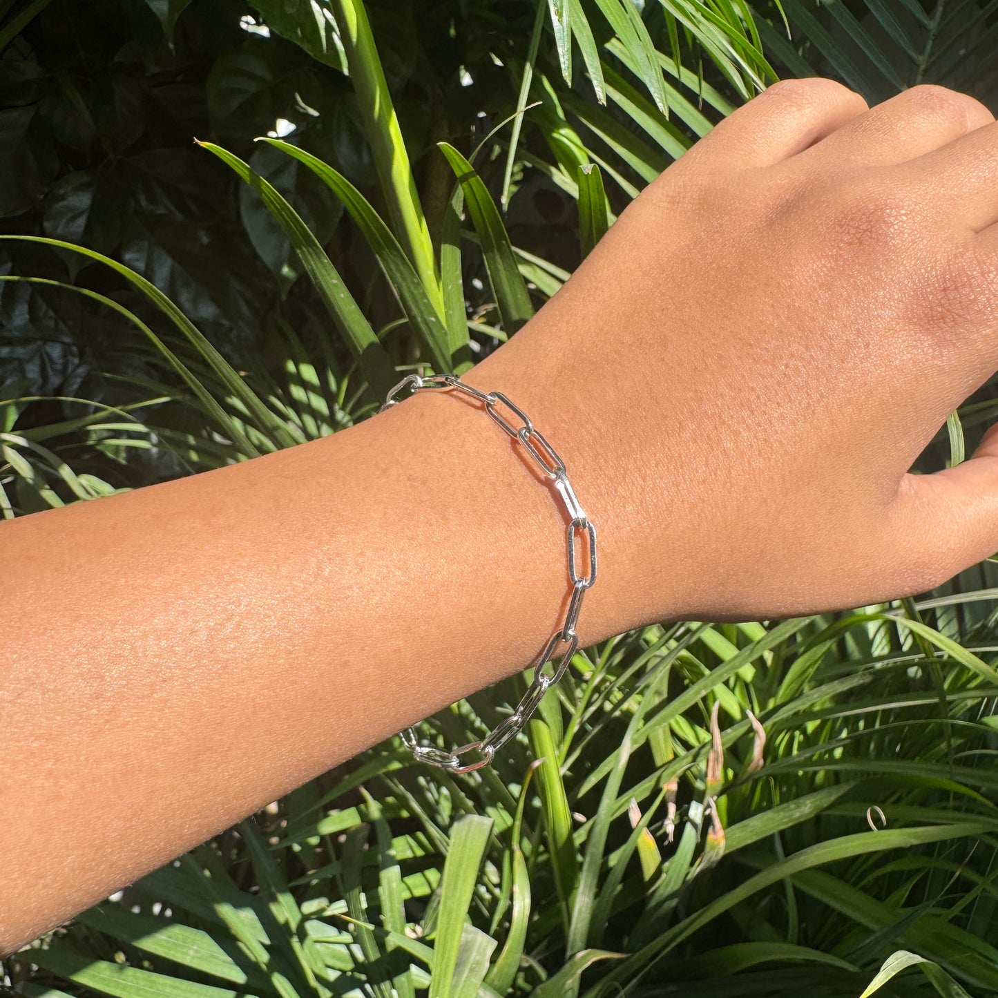 Hand wearing a silver chain bracelet with green foliage in the background