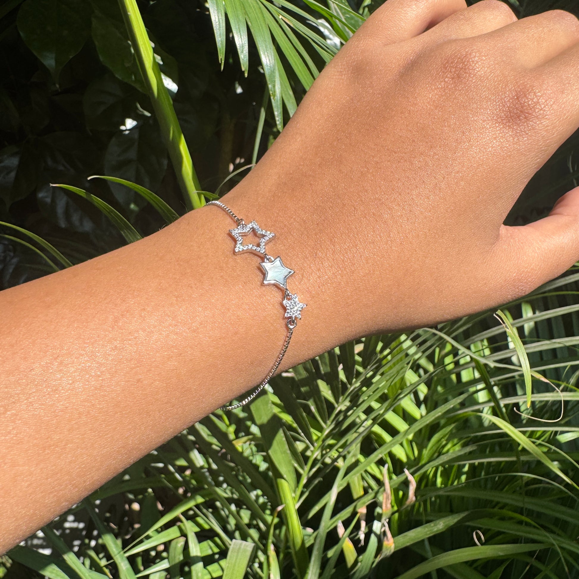 Hand wearing a star-shaped bracelet with green foliage in the background