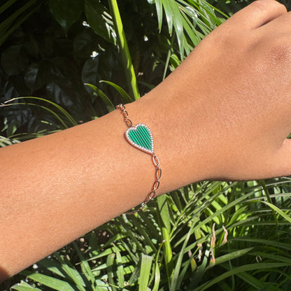 Hand wearing a green heart-shaped bracelet with a leaf design against a green leafy background