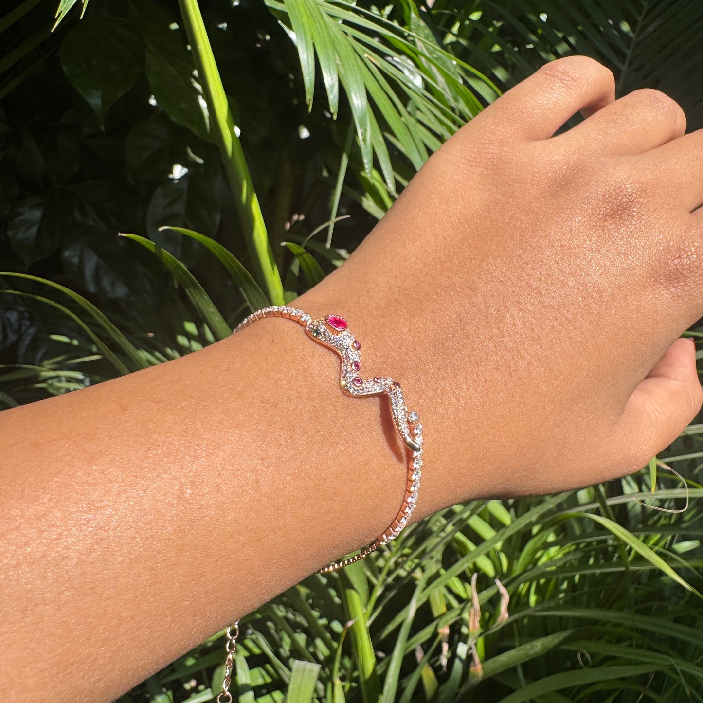 Hand wearing a bracelet with a pink gemstone against a green leafy background