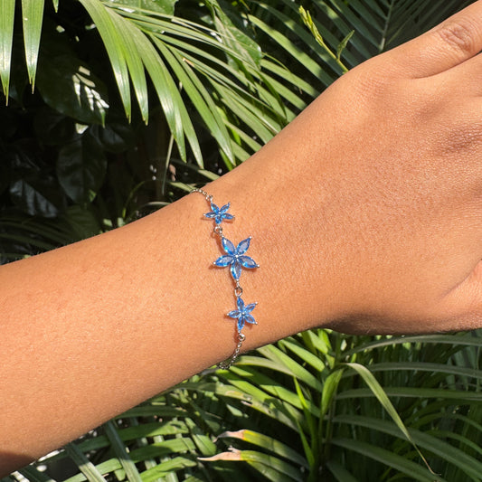 Hand wearing a blue starfish bracelet with green leaves in the background