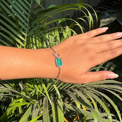 Hand wearing a bracelet with a green charm against a green leafy background