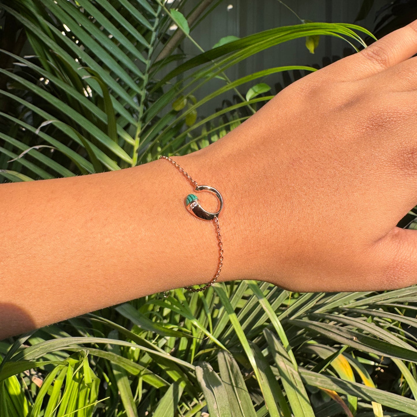 Hand wearing a bracelet with a green gemstone against a green leafy background