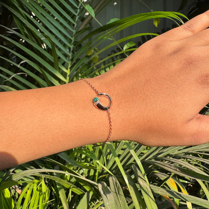 Hand wearing a bracelet with a green gemstone against a green leafy background