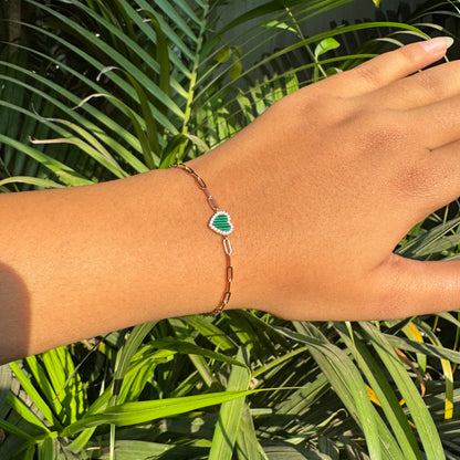 Hand wearing a bracelet with a green heart charm against a green leafy background
