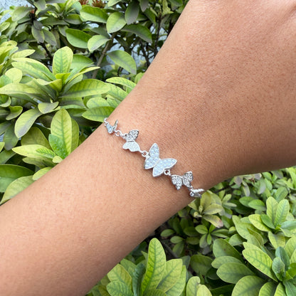Silver butterfly bracelet on a wrist with a green leafy background