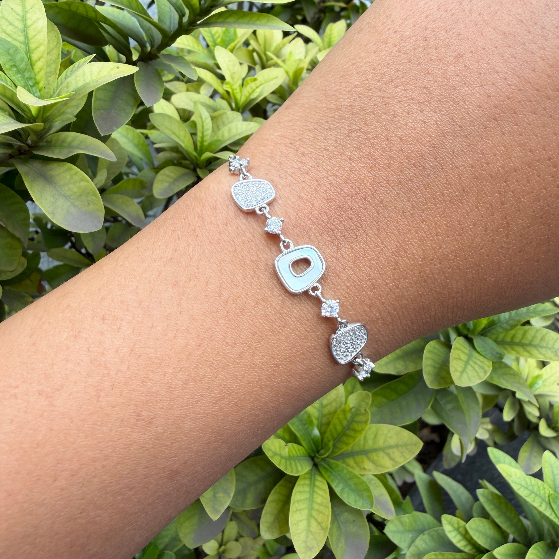 Silver bracelet on a wrist with green foliage in the background