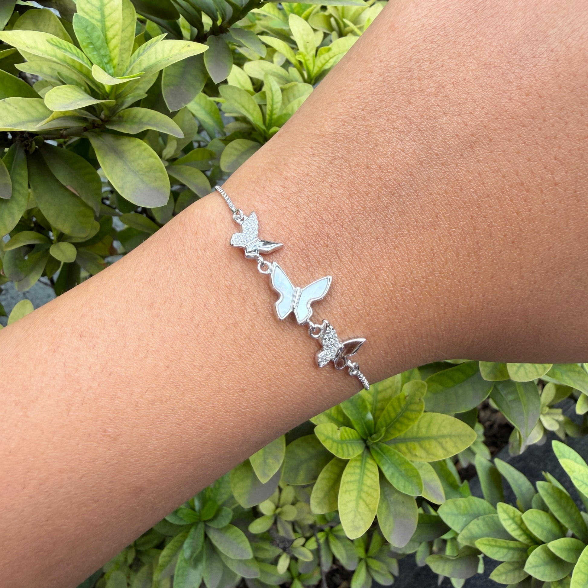 Silver bracelet with butterfly designs on a wrist against a green leafy background