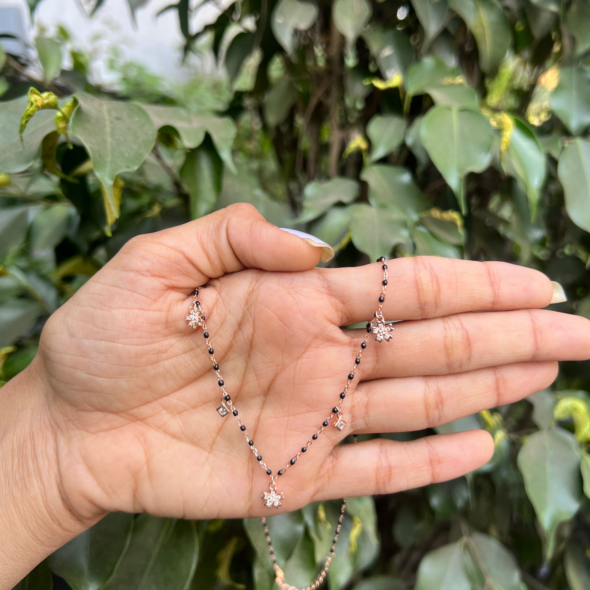 Hand holding a delicate necklace with green foliage in the background