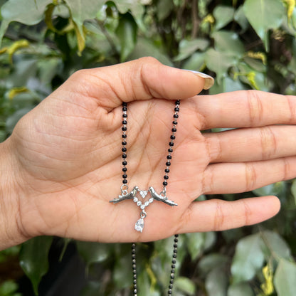 Hand holding a necklace with a silver pendant against a green leafy background