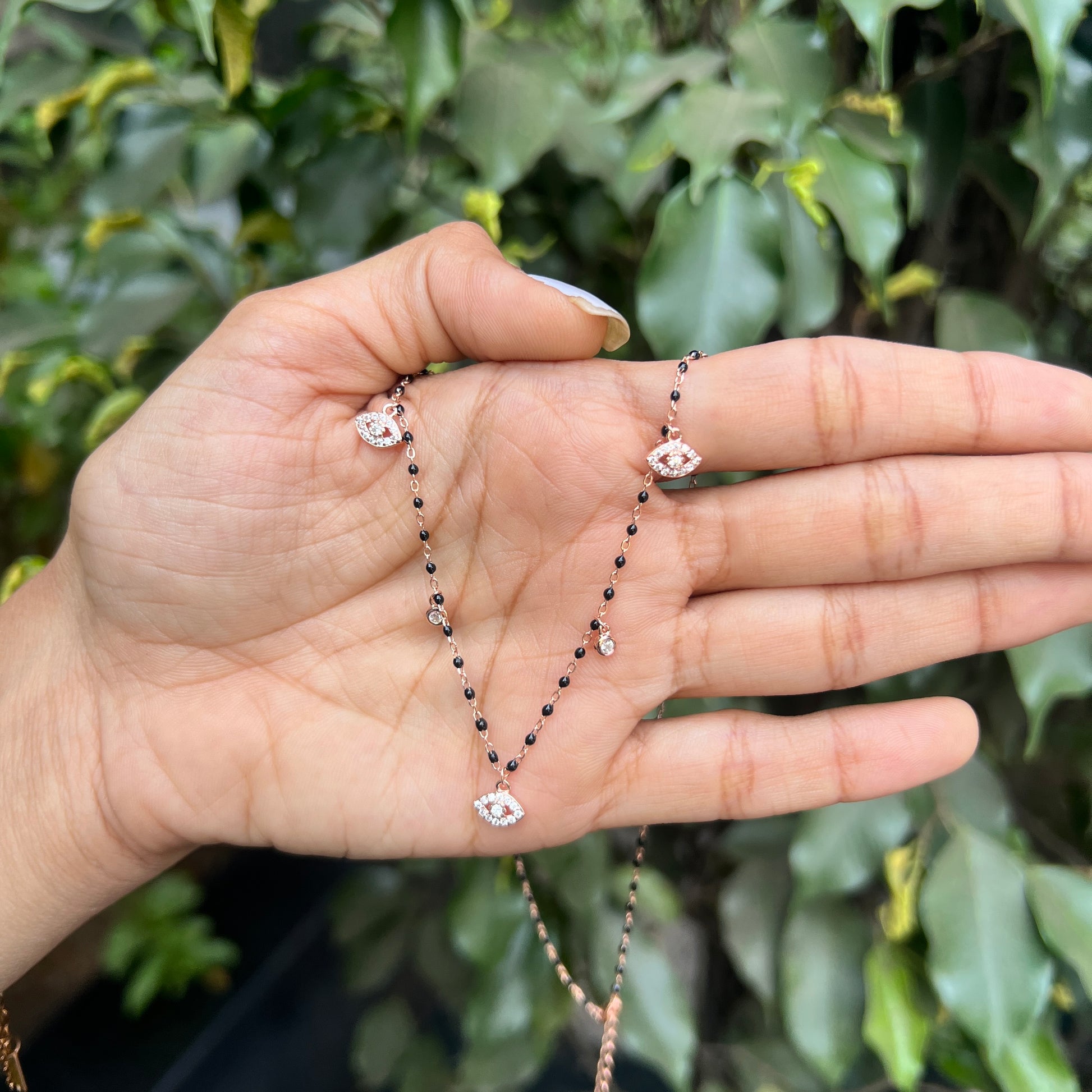 Hand holding a delicate necklace with a green leafy background