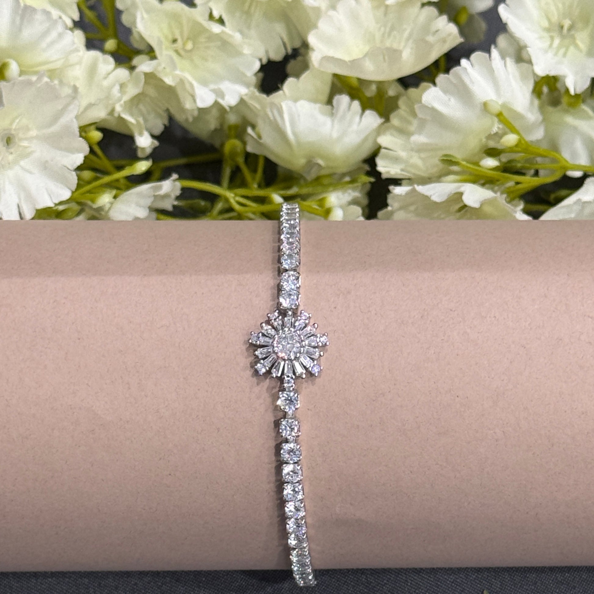 Silver bracelet on a pink cushion with white flowers in the background