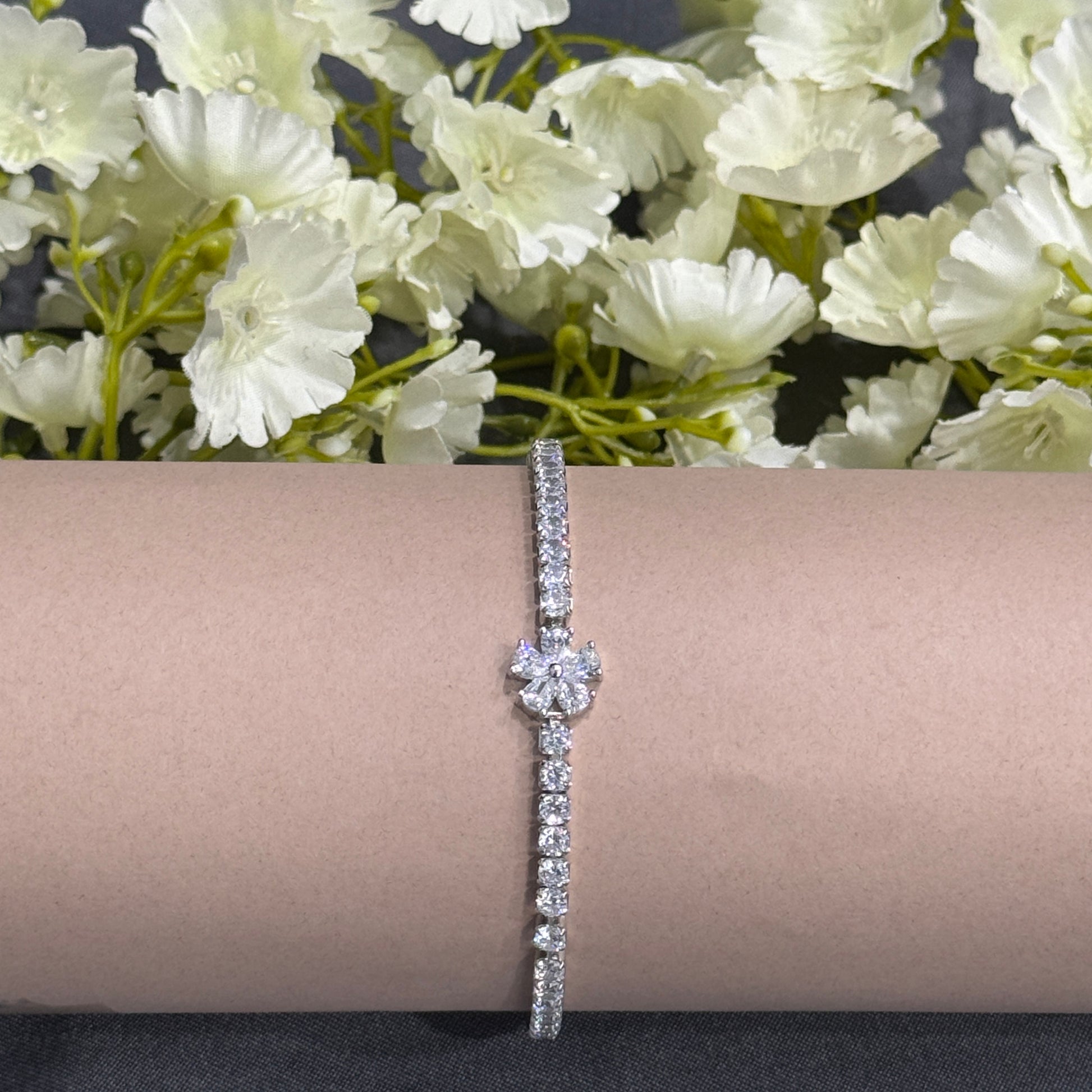 Silver bracelet with floral design on a beige surface with flowers in the background